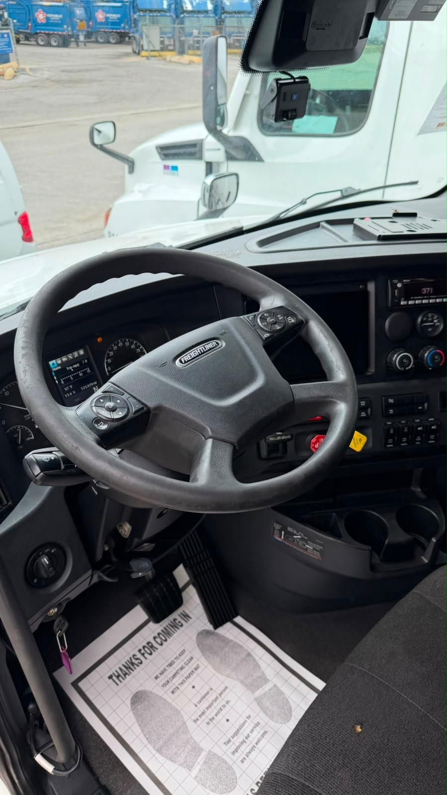 Freightliner steering wheel and dashboard inside a semi cab at a truck yard